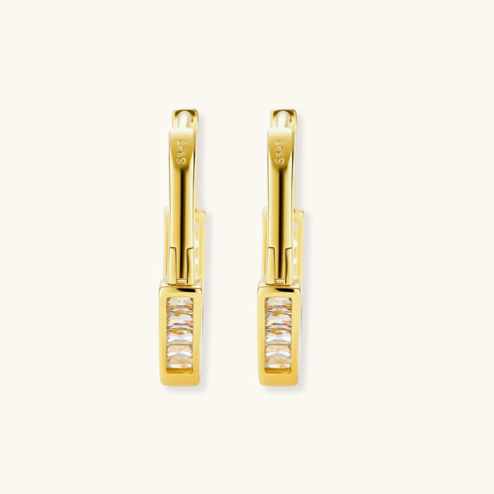 Close-up of gold-plated sterling silver huggie hoop earrings featuring rectangular cubic zirconia stones on neutral background.