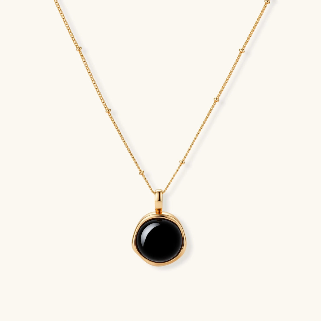 Circular black agate pendant on gold-plated sterling silver chain against cream background, showing modern minimalist design.