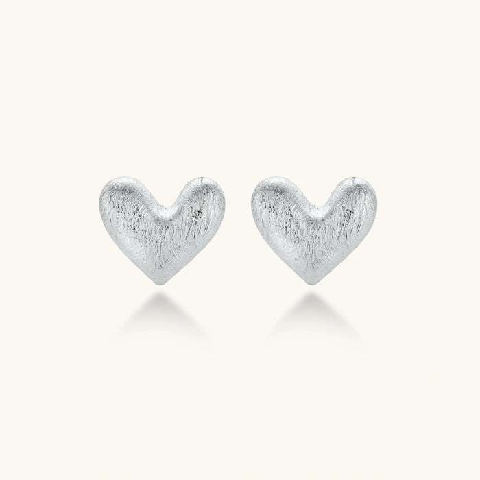 Pair of brushed platinum-plated 925 sterling silver puffy heart stud earrings on a cream background.