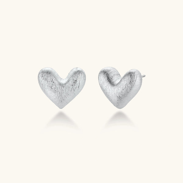 Pair of brushed platinum-plated 925 sterling silver puffy heart stud earrings on a cream background.