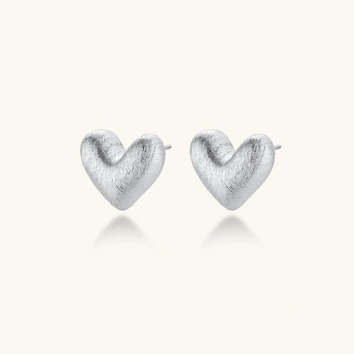 Pair of brushed platinum-plated 925 sterling silver puffy heart stud earrings on a cream background.