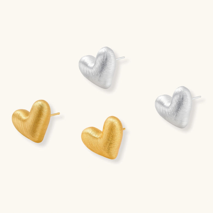 Pair of brushed platinum-plated 925 sterling silver puffy heart stud earrings on a cream background.
