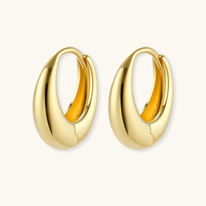 Chunky gold-plated sterling silver huggie hoop earrings with hinged closure mechanism on cream background.