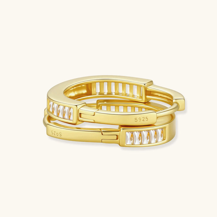 Close-up of gold-plated sterling silver huggie hoop earrings featuring rectangular cubic zirconia stones on neutral background.